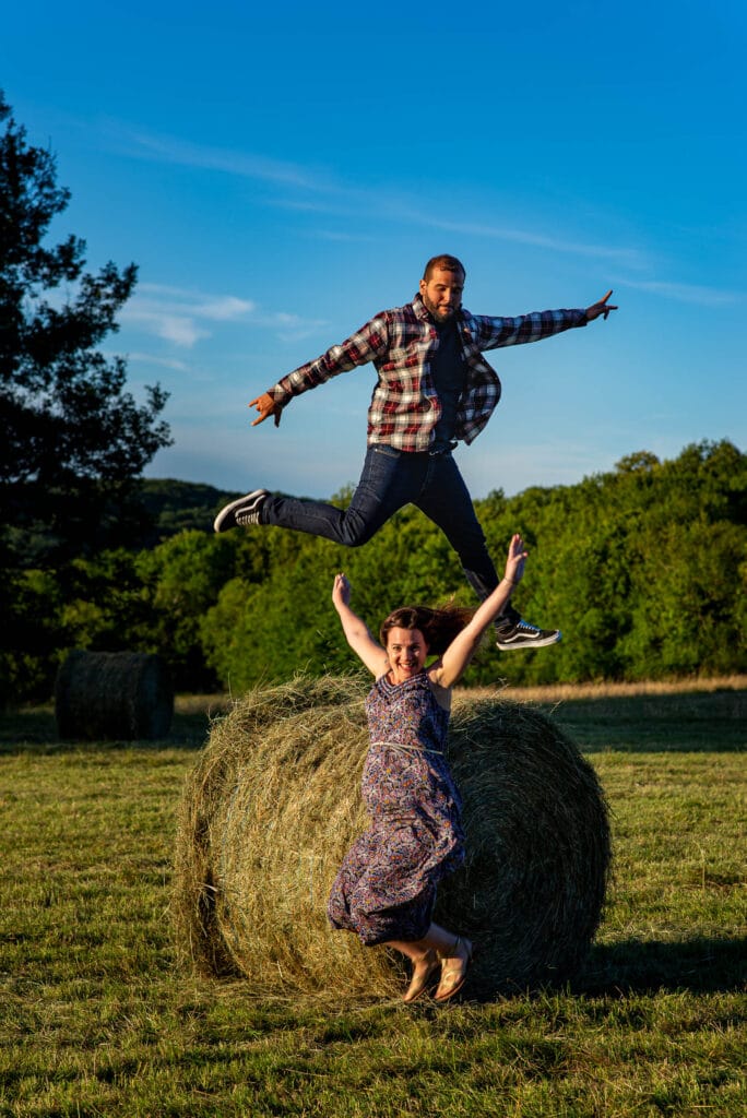 Expectant parents jump for joy on and in front of the haystacks