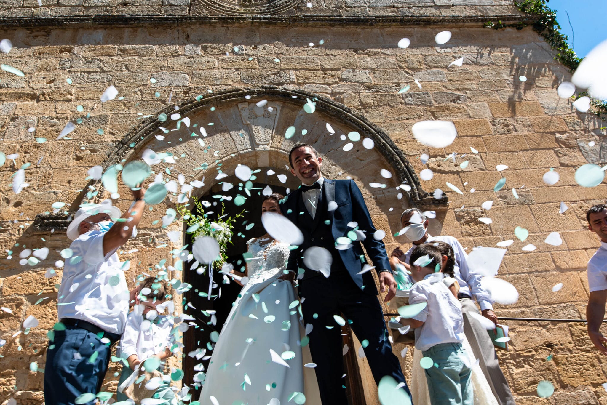 The bride and groom surrounded by green and white petals in front of the church